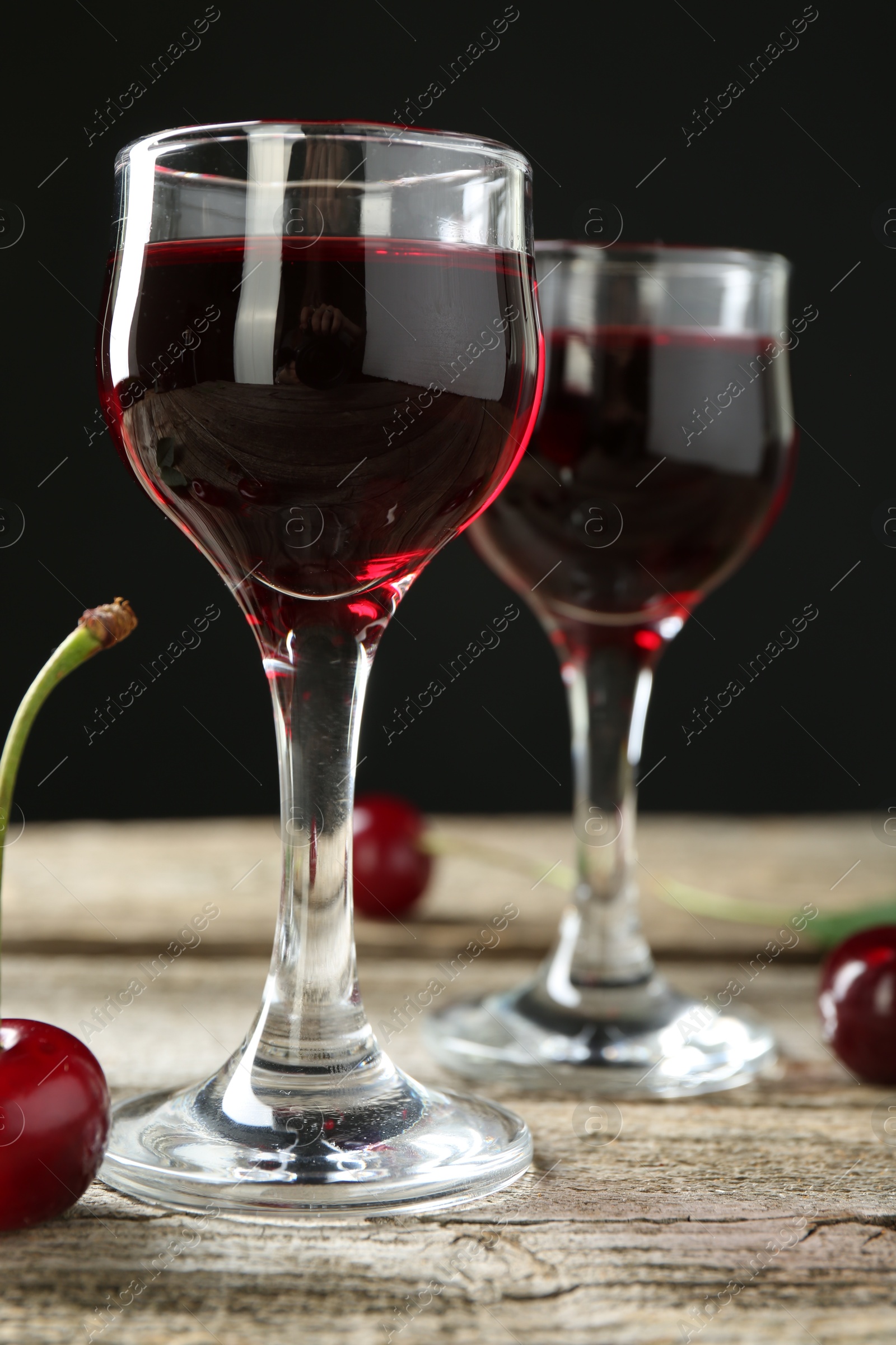 Photo of Glasses of delicious cherry liqueur on wooden table against dark background, closeup