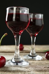 Photo of Glasses of delicious cherry liqueur on wooden table against dark background, closeup