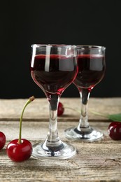 Photo of Glasses of delicious cherry liqueur and juicy berries on wooden table against dark background