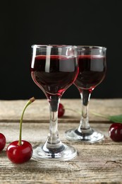 Glasses of delicious cherry liqueur and juicy berries on wooden table against dark background