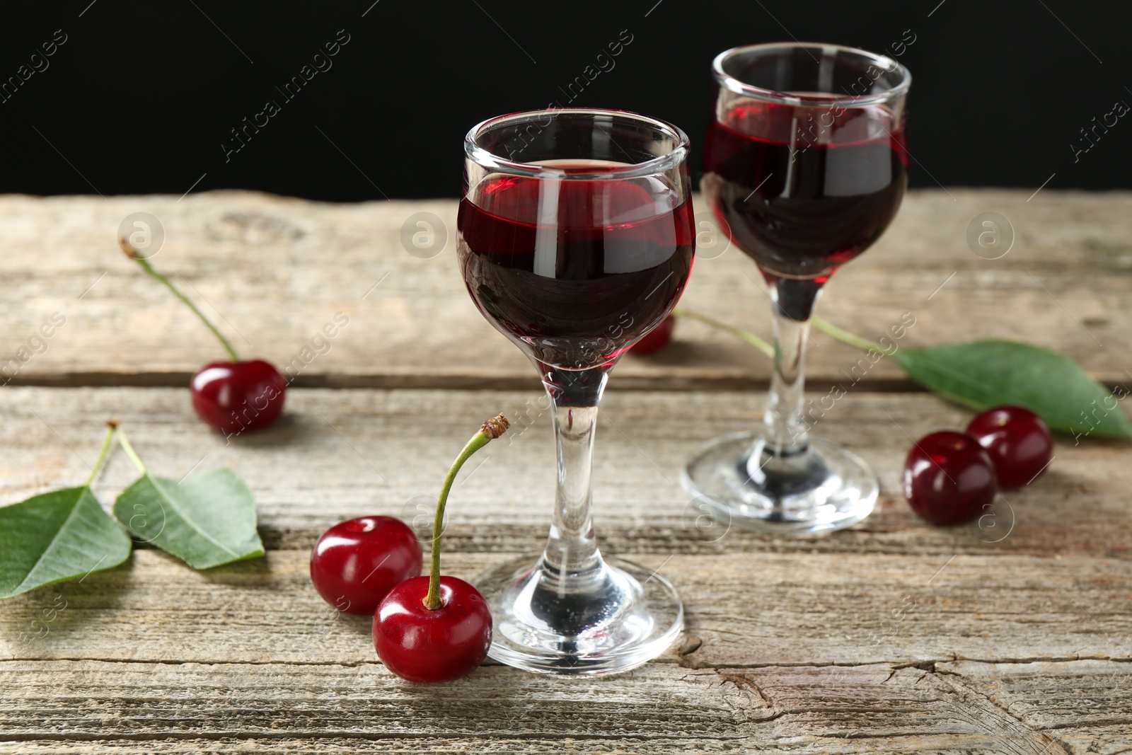 Photo of Glasses of delicious cherry liqueur and juicy berries on wooden table