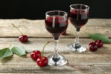 Photo of Glasses of delicious cherry liqueur and juicy berries on wooden table