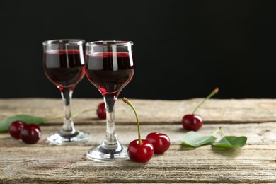 Photo of Glasses of delicious cherry liqueur on wooden table against dark background, space for text