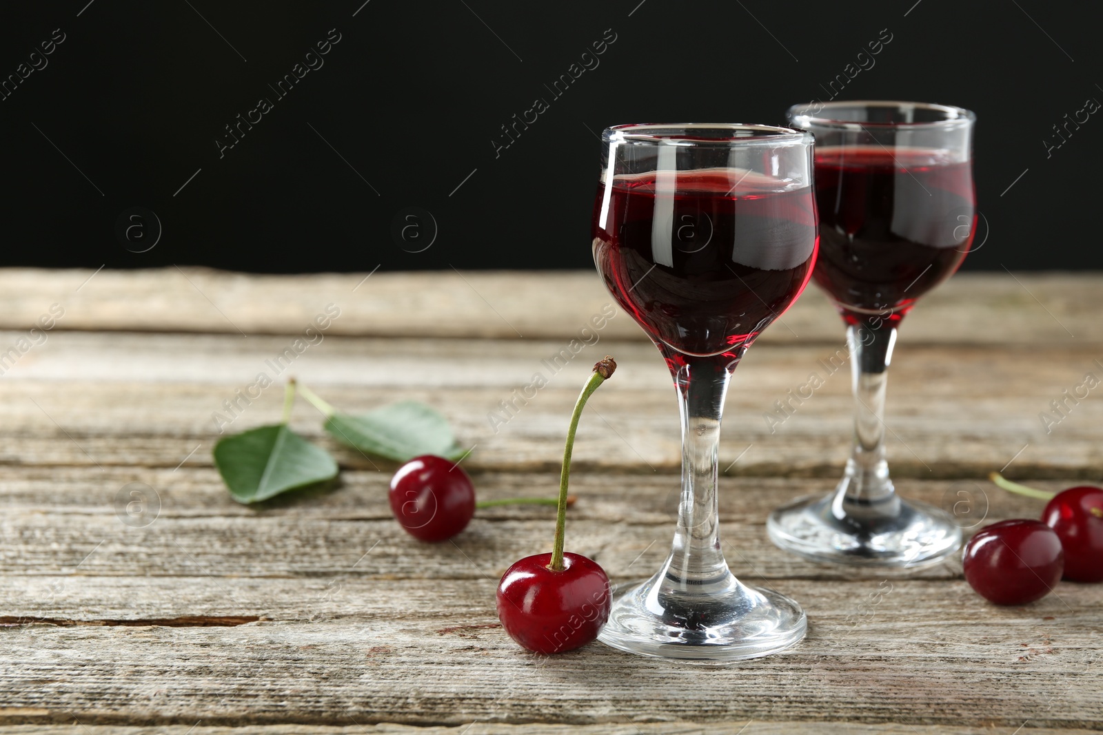 Photo of Glasses of delicious cherry liqueur on wooden table against dark background, space for text