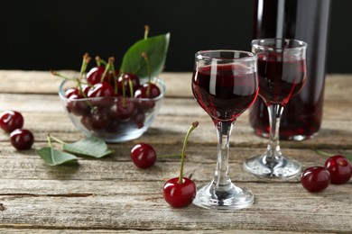 Photo of Bottle and glasses of delicious cherry liqueur with juicy berries on wooden table