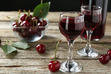Photo of Bottle and glasses of delicious cherry liqueur with juicy berries on wooden table, closeup