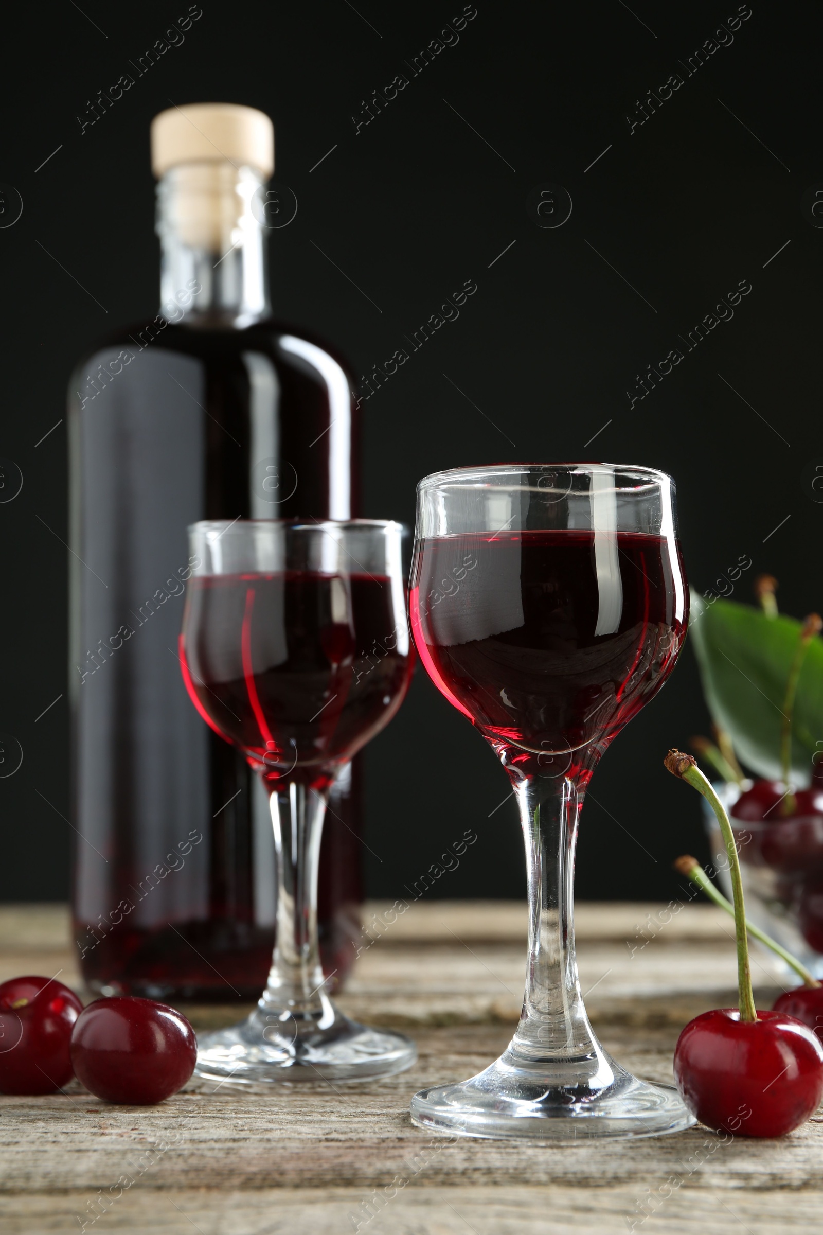 Photo of Bottle and glasses of delicious cherry liqueur with juicy berries on wooden table against dark background