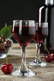 Bottle and glasses of delicious cherry liqueur with juicy berries on wooden table, closeup