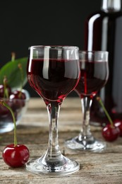 Photo of Bottle and glasses of delicious cherry liqueur with juicy berries on wooden table, closeup