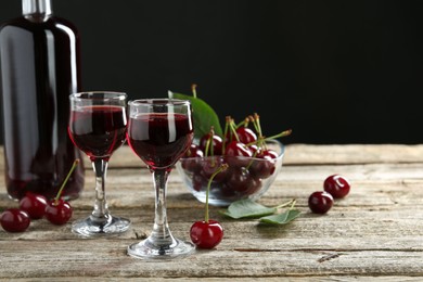 Photo of Bottle and glasses of delicious cherry liqueur with juicy berries on wooden table against dark background, space for text