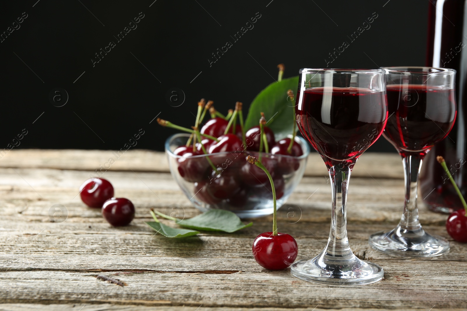 Photo of Glasses of delicious cherry liqueur on wooden table against dark background, space for text