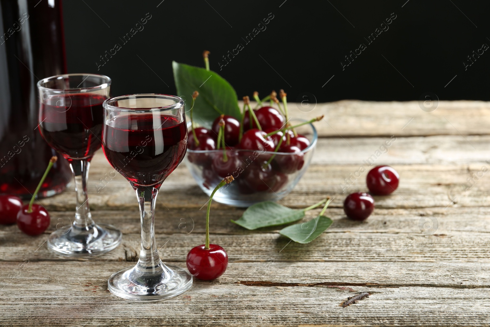 Photo of Bottle and glasses of delicious cherry liqueur with juicy berries on wooden table