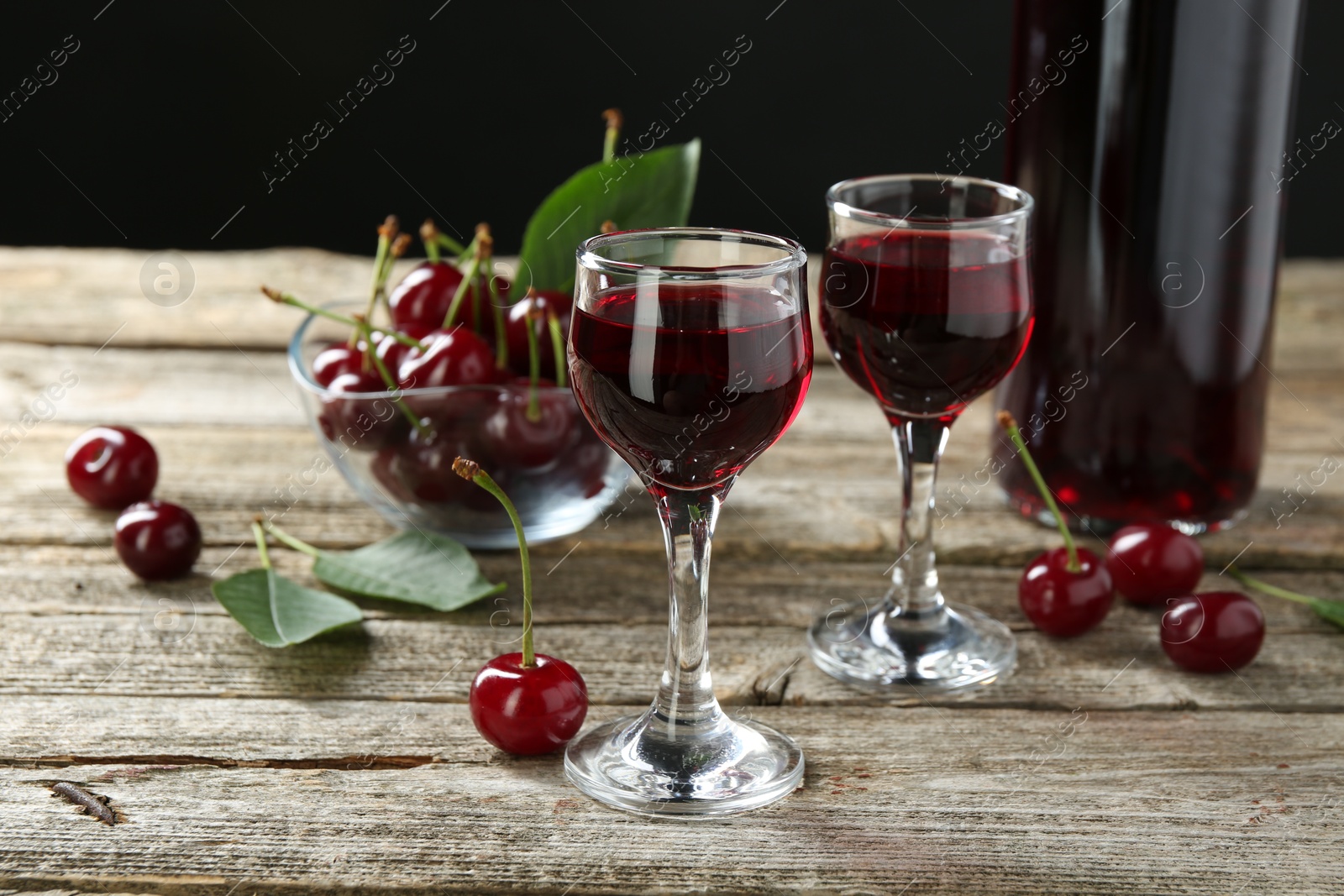 Photo of Bottle and glasses of delicious cherry liqueur with juicy berries on wooden table