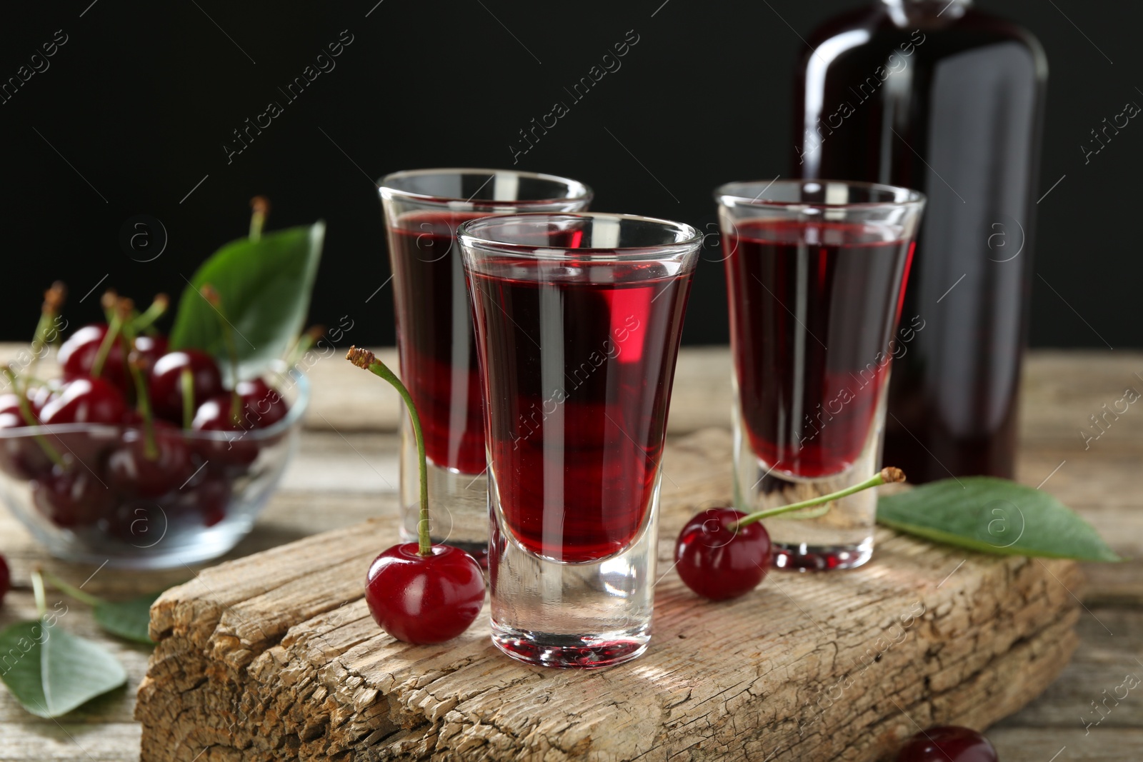 Photo of Bottle and shot glasses of delicious cherry liqueur with juicy berries on wooden table