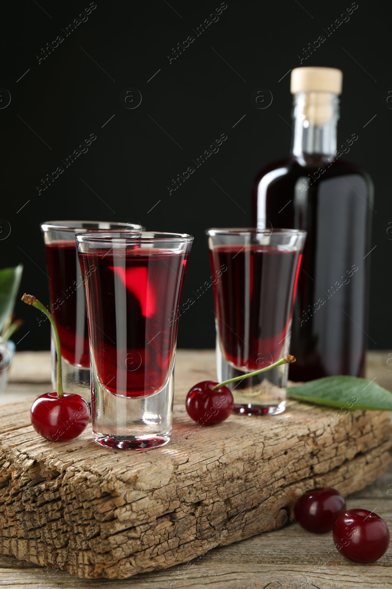 Photo of Bottle and glasses of delicious cherry liqueur with juicy berries on wooden table against dark background