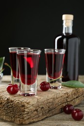 Photo of Bottle and glasses of delicious cherry liqueur with juicy berries on wooden table against dark background
