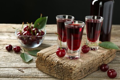 Photo of Bottle and shot glasses of delicious cherry liqueur with juicy berries on wooden table