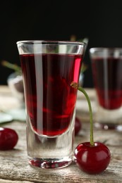 Photo of Shot glass of delicious cherry liqueur and juicy berry on wooden table, closeup