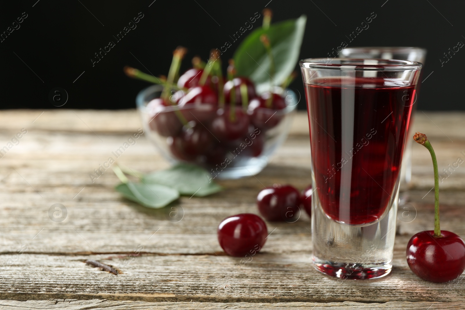 Photo of Shot glasses of delicious cherry liqueur and fresh berries on wooden table, closeup. Space for text