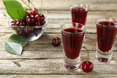 Photo of Shot glasses of delicious cherry liqueur and juicy berries on wooden table, closeup