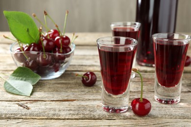 Photo of Bottle and shot glasses of delicious cherry liqueur with juicy berries on wooden table
