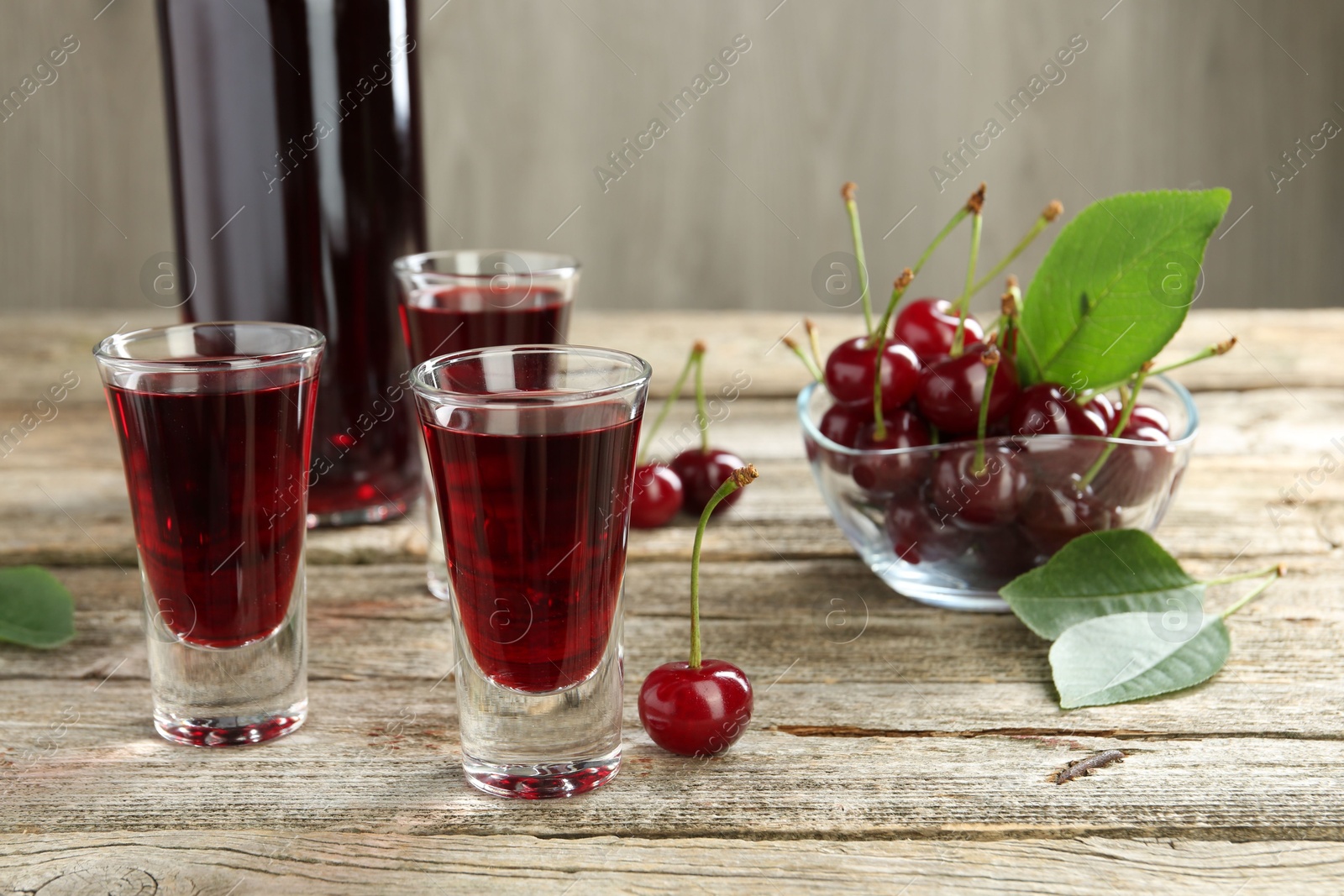 Photo of Bottle and shot glasses of delicious cherry liqueur with juicy berries on wooden table