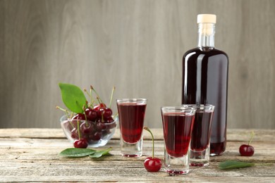 Photo of Bottle and shot glasses of delicious cherry liqueur with juicy berries on wooden table, space for text