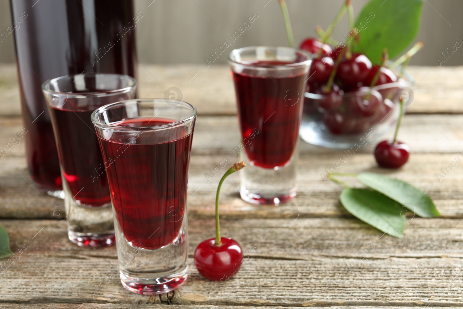 Photo of Bottle and shot glasses of delicious cherry liqueur with juicy berries on wooden table, closeup