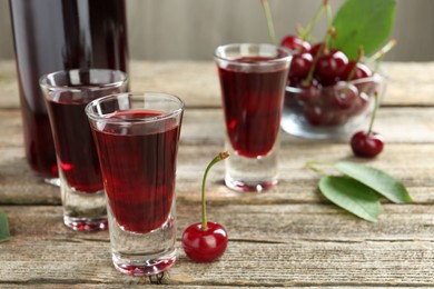 Photo of Bottle and shot glasses of delicious cherry liqueur with juicy berries on wooden table, closeup