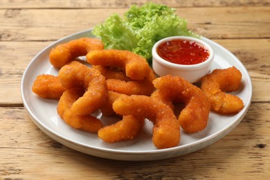 Photo of Tasty breaded fried shrimps served with sauce on wooden table, closeup