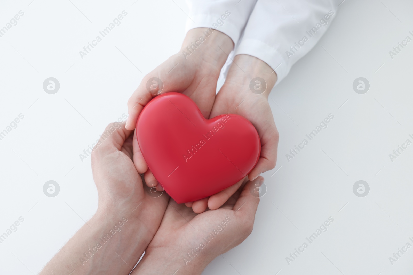 Photo of Doctor and patient holding red heart on white background, top view