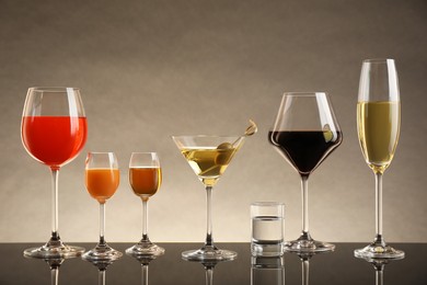 Photo of Glasses with different alcoholic drinks on table against beige background