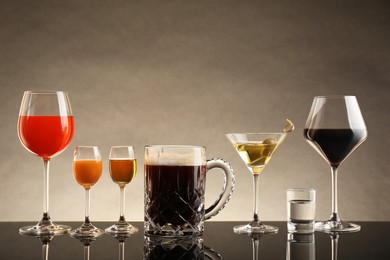 Glasses with different alcoholic drinks on table against beige background