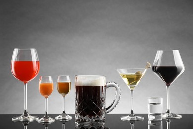 Glasses with different alcoholic drinks on table against light grey background