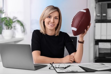 Photo of Smiling woman with american football ball at table in office