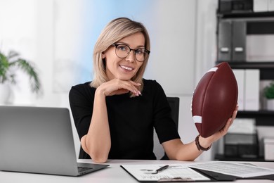 Photo of Smiling woman with american football ball at table in office