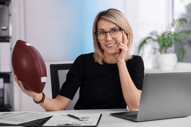 Smiling woman with american football ball at table in office