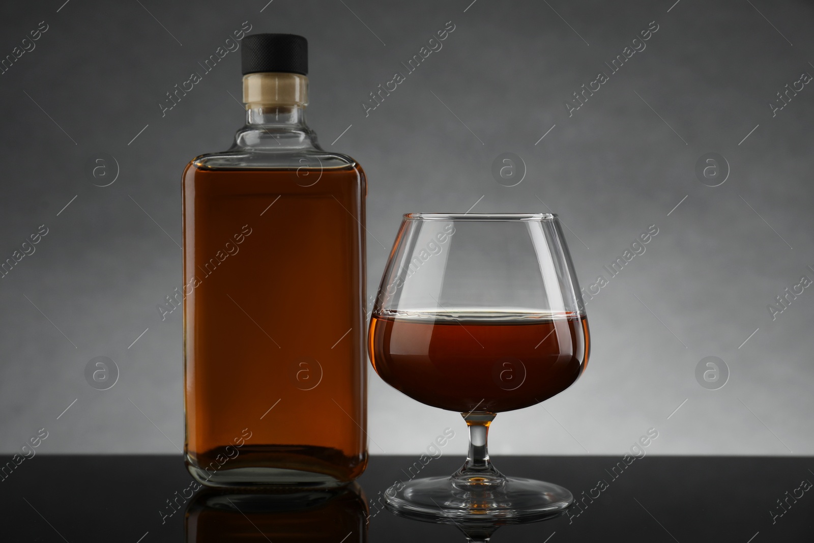 Photo of Bottle and glass with whiskey on table against gray background