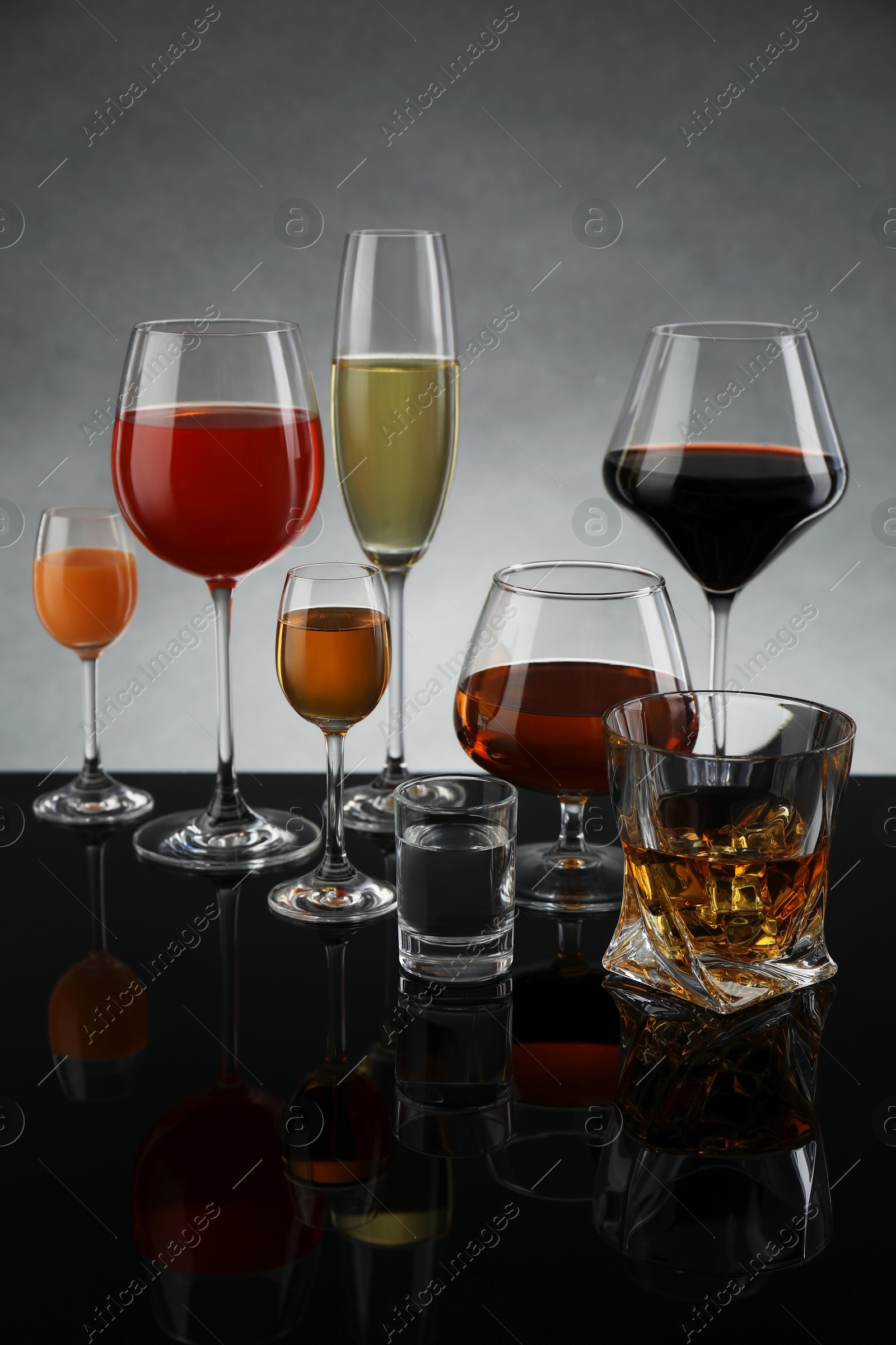 Photo of Glasses with different alcoholic drinks on table against gray background