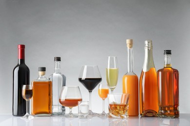 Bottles and glasses with different alcoholic drinks on white table against light background