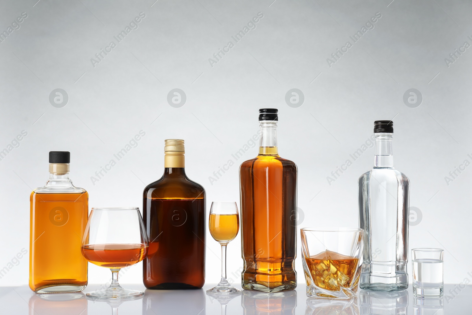 Photo of Bottles and glasses with different alcoholic drinks on white table against light background