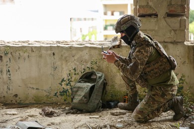 Photo of Military mission. Soldier in uniform with drone controller inside abandoned building, space for text