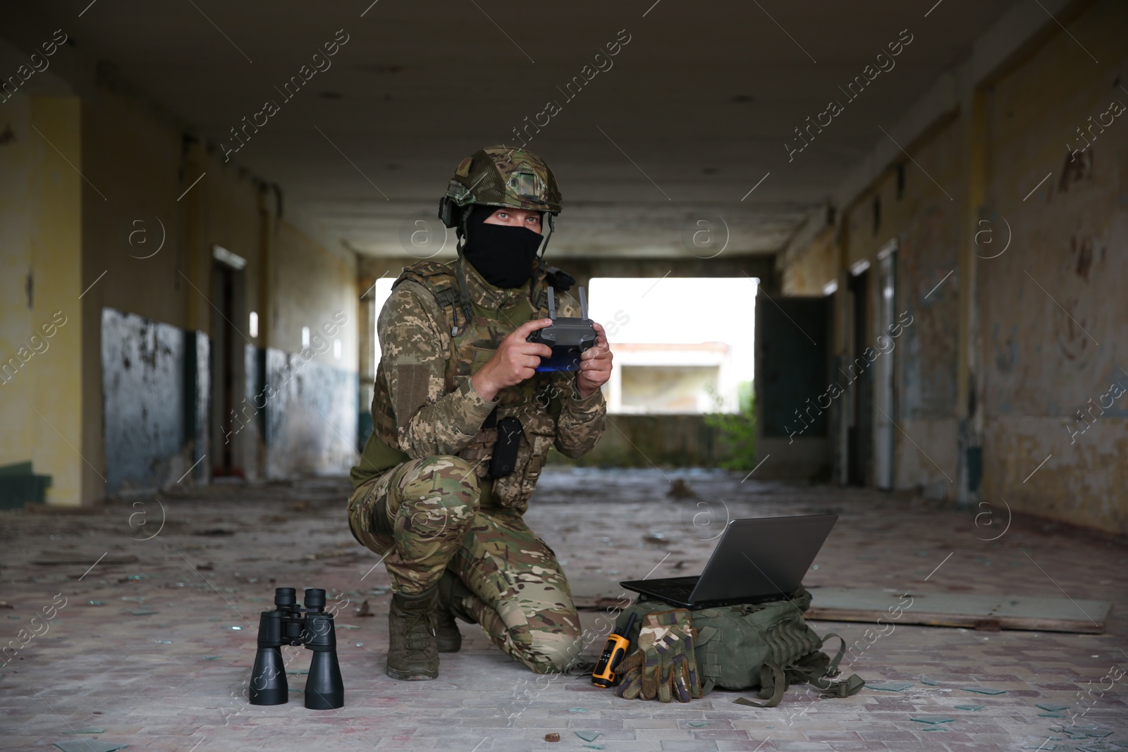 Photo of Military mission. Soldier in uniform with drone controller, laptop and binoculars inside abandoned building