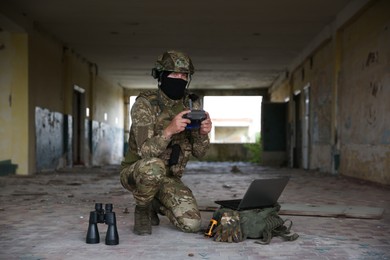 Military mission. Soldier in uniform with drone controller, laptop and binoculars inside abandoned building