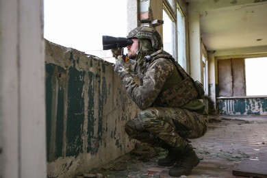 Photo of Military mission. Soldier in uniform with binoculars inside abandoned building