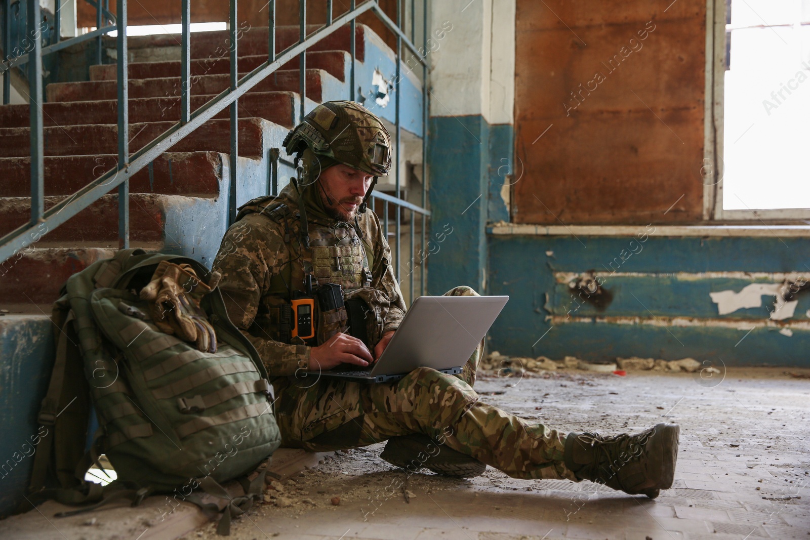 Photo of Military mission. Soldier in uniform using laptop inside abandoned building