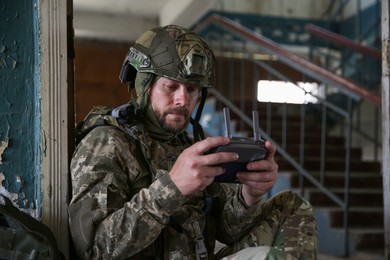 Photo of Military mission. Soldier in uniform with drone controller inside abandoned building