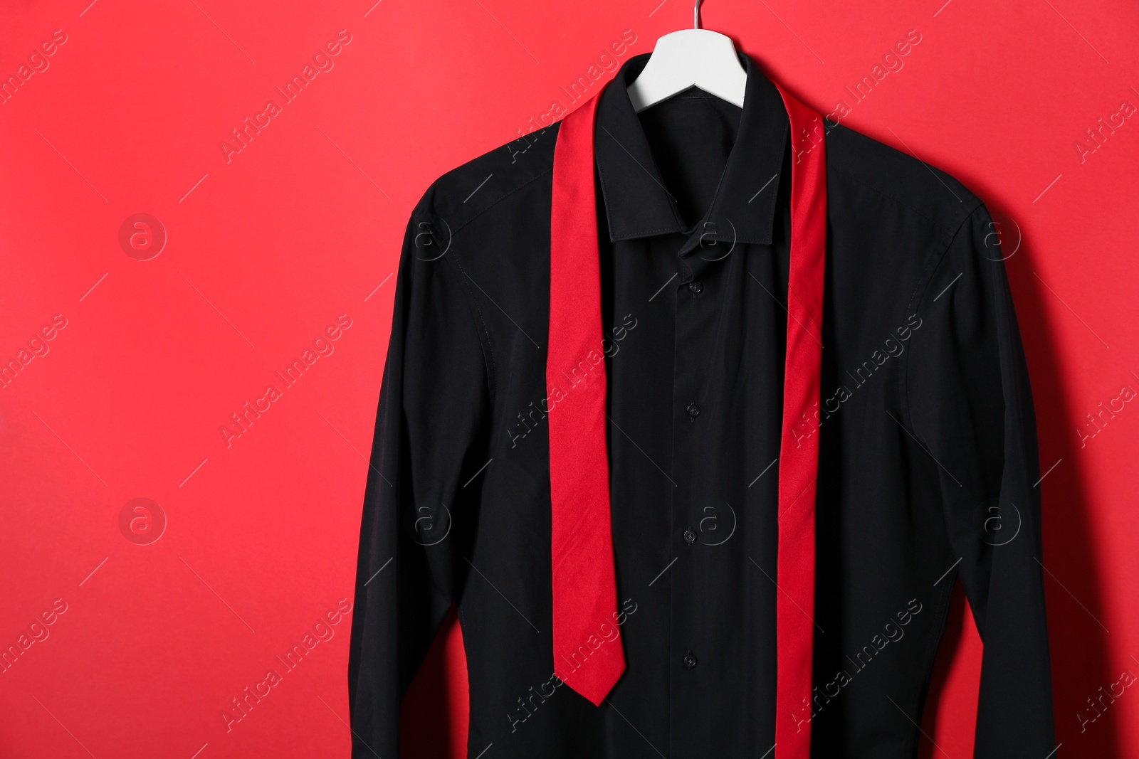 Photo of Hanger with shirt and necktie on red background. Space for text