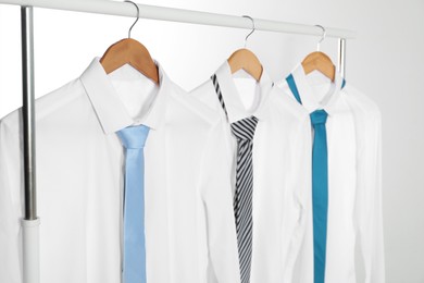 Photo of Hangers with white shirts and neckties on clothing rack against light background, closeup