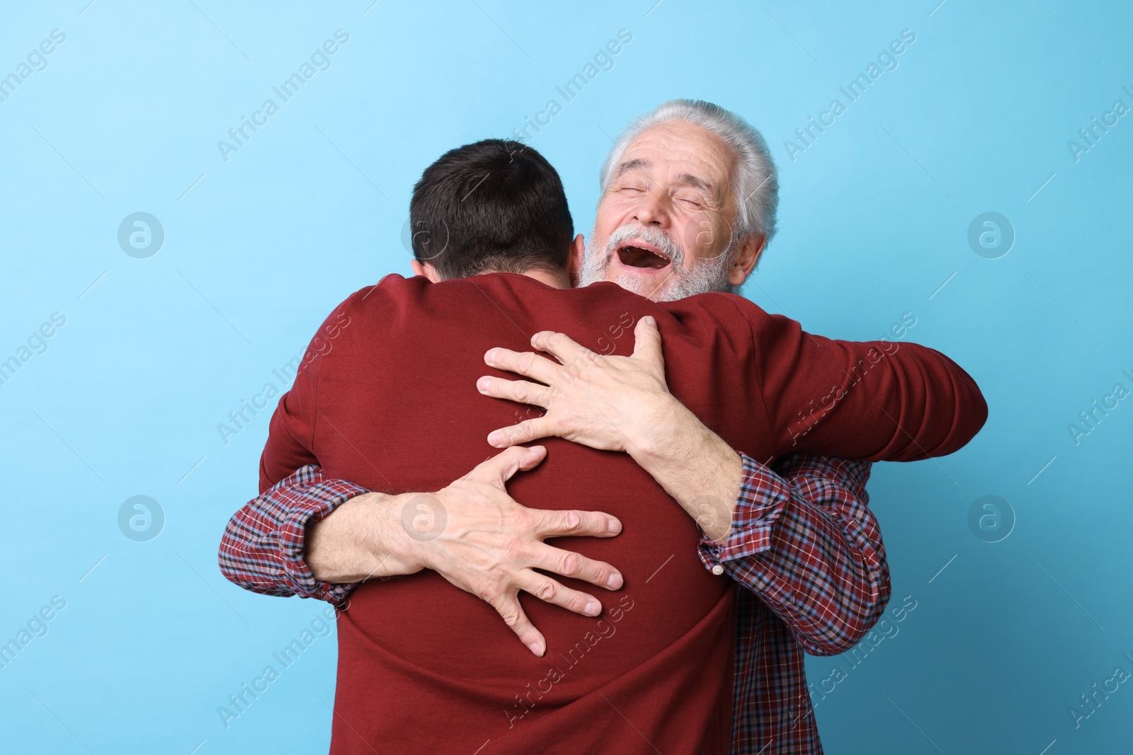 Photo of Happy dad and his son hugging on light blue background